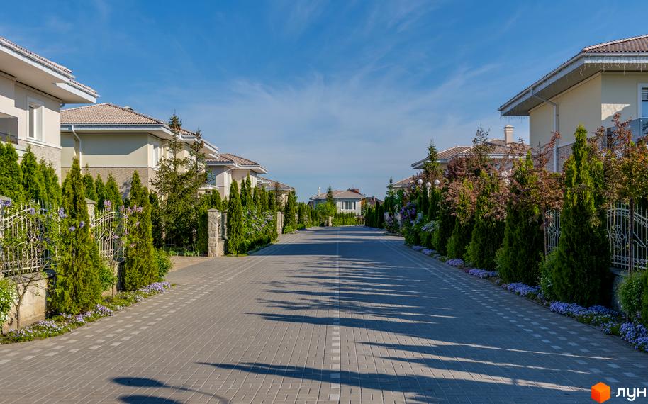 Вулиця в Котеджному містечку Золоче Прованс з будинками по обидва боки. Навколо будинків висаджені дерева та кущі.