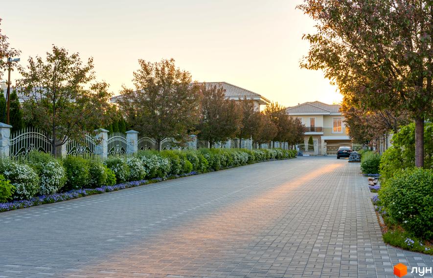 Вигляд на Котеджне містечко Золоче Прованс: двоповерхові будинки з черепичною покрівлею, зелені насадження та дорога з тротуарної плитки.