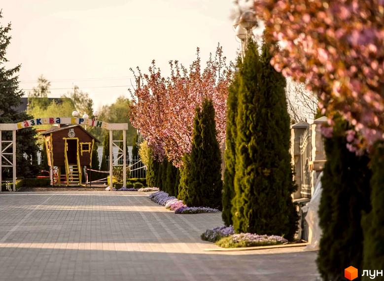 Вигляд на Котеджне містечко Золоче Прованс з алеєю з туй та квітучих дерев. На задньому плані дитячий майданчик.