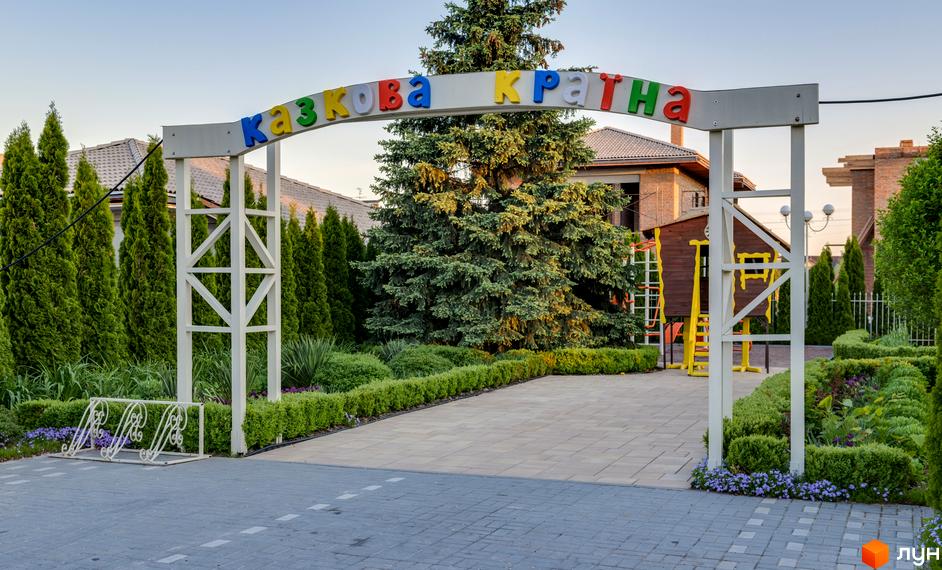 Вхідна група Котеджного містечка Золоче Прованс з аркою, прикрашеною написом. На території доглянуті газони, дерева та бруківка.