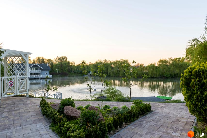 Котеджне містечко Золоче Прованс з будинками біля озера. На передньому плані бруківка та зелені насадження, на задньому - котеджі.