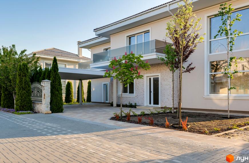 Двоповерховий будинок в КМ Золоче Прованс з білими стінами та скляним балконом. На території бруківка, дерева та зелені насадження.