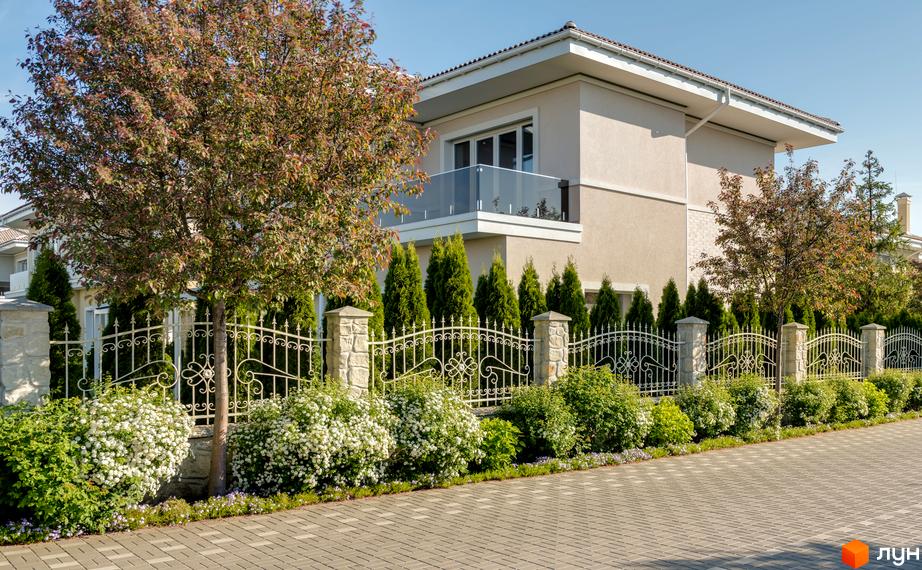 Вигляд будинку в Котеджному містечку Золоче Прованс з балконом. Навколо будинку зелені насадження та кована огорожа.