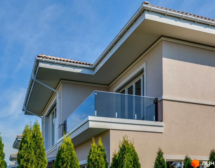 Фасад будинку в Містечку котеджів Золоче Прованс з балконом та скляним огородженням, поруч зелені насадження та блакитне небо.