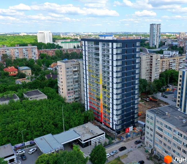 Житловий комплекс Магістр - це висотна будівля з темно-сірим фасадом та яскравими вертикальними смугами жовтого, помаранчевого та червоного кольорів. На прибудинковій території видно дорогу з автомобілями та зелені насадження.