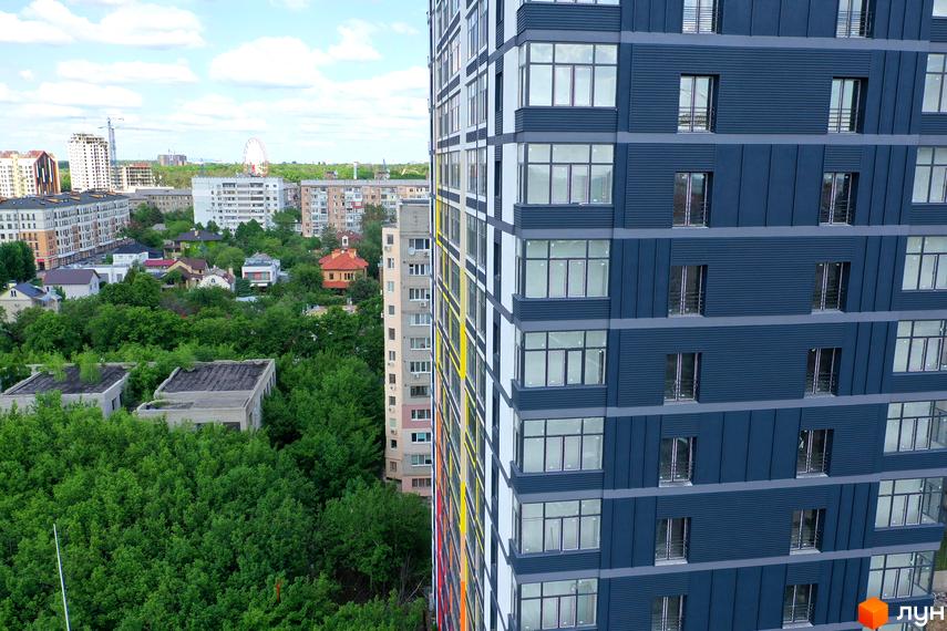 Зовнішній вигляд новобудови ЖК Магістр з сірими фасадами та великими вікнами, оточеної зеленню та іншими будівлями.