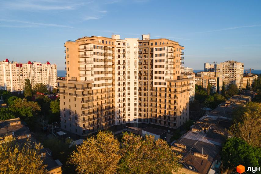 Висотна будівля ЖК Мілос з балконами та панорамними вікнами. Навколо будинку зелені дерева та інші будівлі.