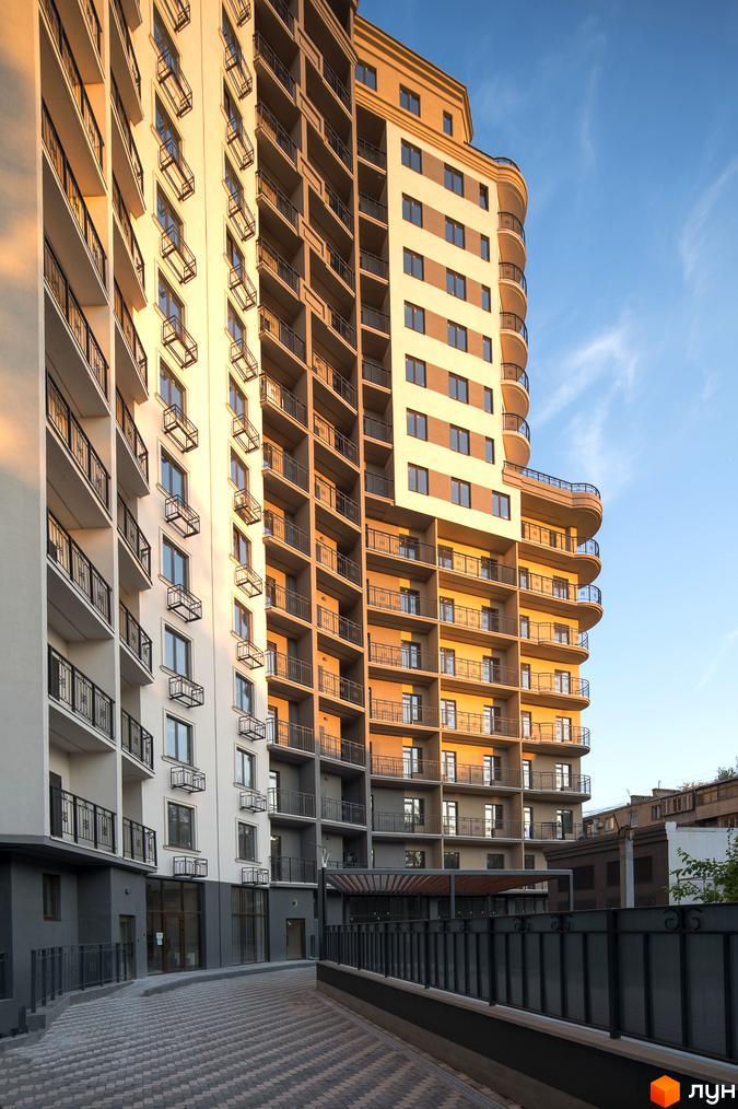 Висотна будівля ЖК Мілос з балконами та панорамними вікнами. На передньому плані бруківка та металева огорожа.