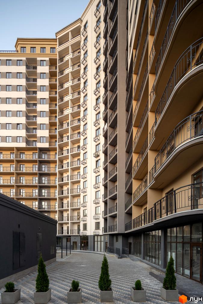 Житловий комплекс Мілос з фасадами світлих відтінків. На першому поверсі будівлі розташовані комерційні приміщення. На прибудинковій території висаджені декоративні дерева.