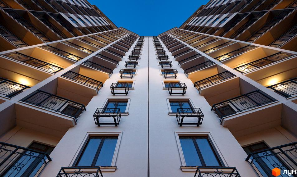 Вид знизу вгору на будівлю ЖК Мілос. Висотна будівля з балконами та вікнами на тлі синього неба.