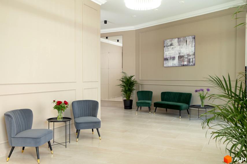 Інтер'єр холу в ЖК Мілос. Світлі стіни з декоративними панелями, м'які дивани та крісла. Просторий хол з рослинами та картинами.
