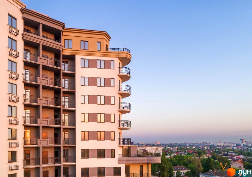 Висотна будівля житлового комплексу Мілос з балконами та панорамними вікнами. На задньому плані видно міську забудову та блакитне небо.