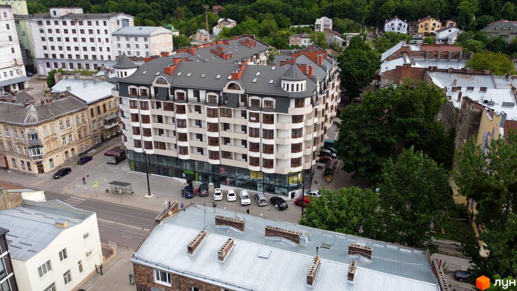 Житловий комплекс Львівський дворик - це багатоповерхова новобудова з балконами та еркерними вікнами. Навколо будівлі розташовані дерева та сусідні будинки.