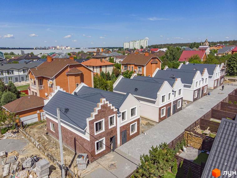 Дуплекси Lucky Home з темно-сірими дахами та фасадами з цегли і світлої штукатурки. Поруч вулиця з бруківки та зелені насадження.