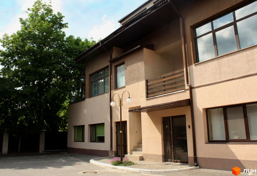 Зображення фасаду будинку ЖК Таунхаус „Холодногірський“. Бежевий будинок з великими вікнами та балконом. Поруч зелені дерева та доріжка.