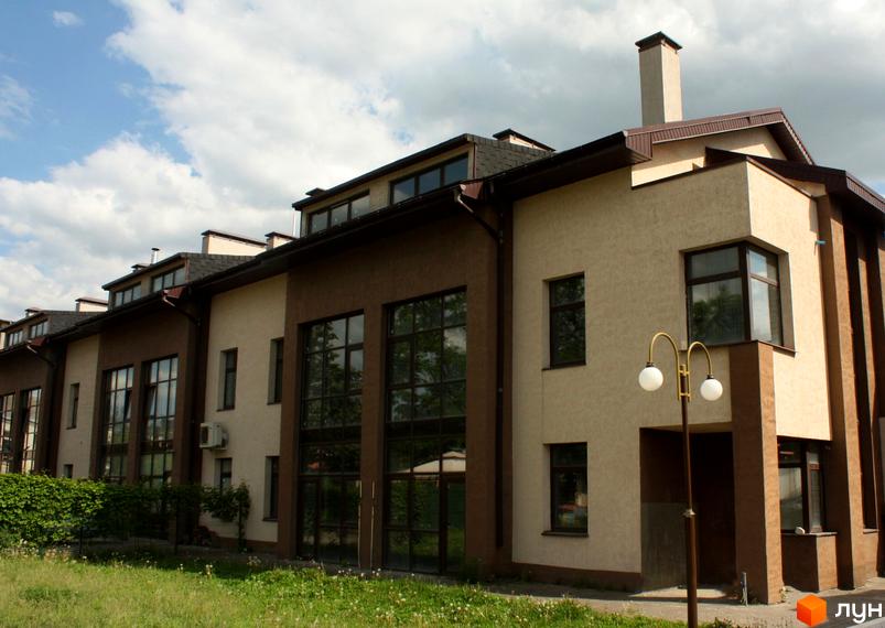 Зовнішній вигляд таунхауса Холодногірський. Будинок має світлий фасад з великими вікнами. Поруч газон та ліхтар.