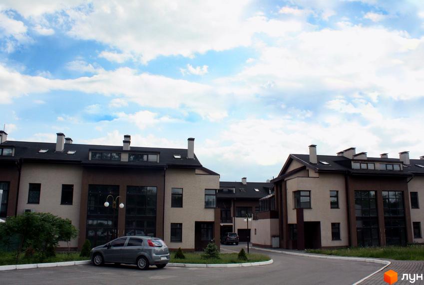 Зображення житлового комплексу таунхаус „Холодногірський“. На фото видно будинки з темною покрівлею та світлими фасадами. Поруч з будинками розташована прибудинкова територія з автомобілем.