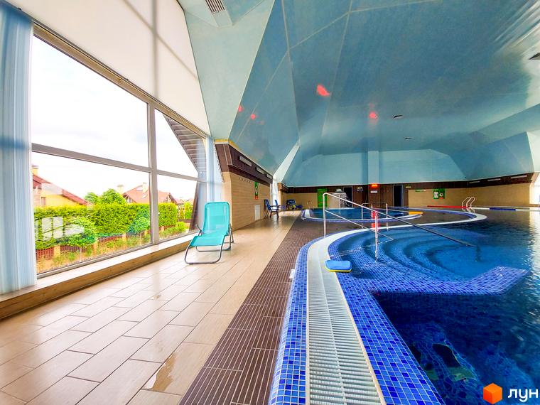 Критий басейн в котеджному містечку Северинівка. Просторий басейн з блакитною плиткою та великими вікнами з видом на зелені насадження.