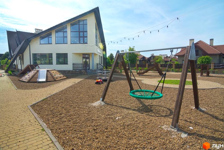 Будинок з великими вікнами та дитячим майданчиком. Поруч розташовані гойдалки та гірка.
