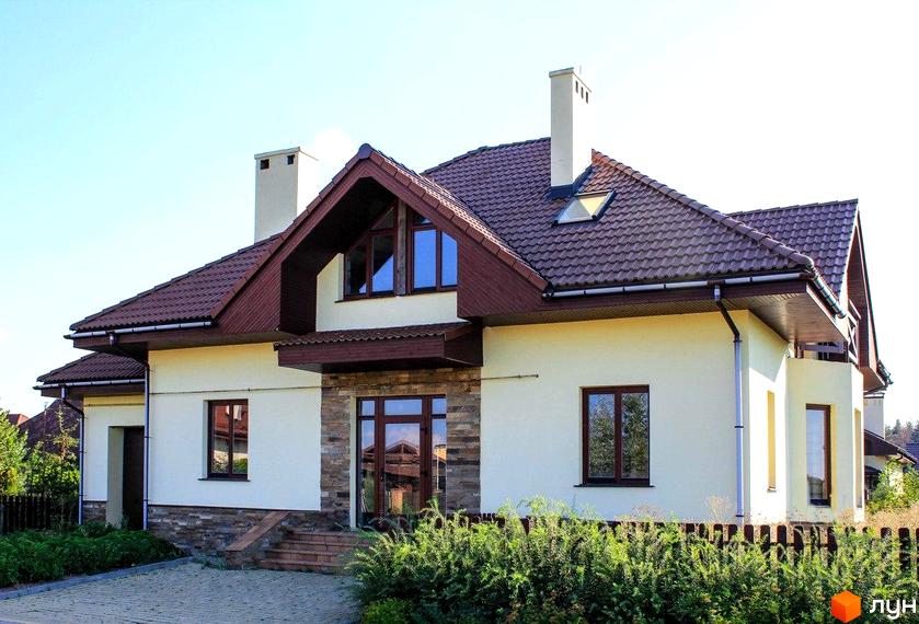 Зображення будинку в Котеджному містечку Северинівка. Будинок з коричневою черепицею та світлими стінами, перед будинком зелені кущі та доріжка.