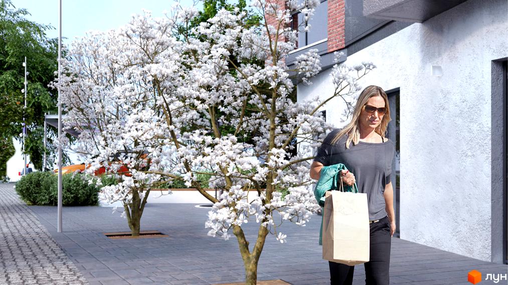 Зображення фасаду та прибудинкової території Житлового комплексу Ярославенка. На передньому плані дерева з білими квітами, тротуарна плитка.