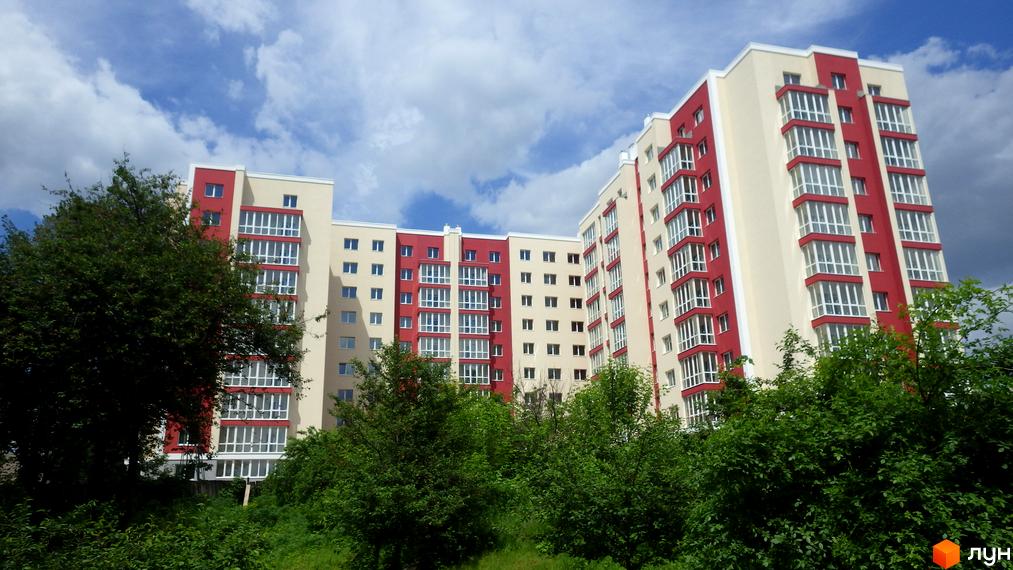 Житловий комплекс Мрія: багатоповерховий будинок з кремово-червоним фасадом та заскленими балконами. На передньому плані зелені насадження.