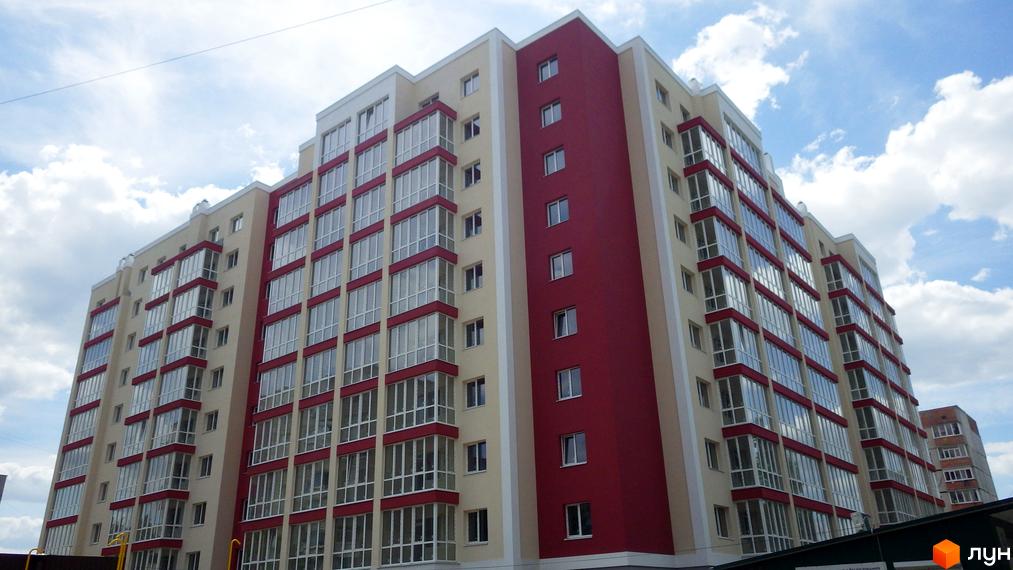 Новобудова Мрія: багатоповерховий будинок з червоно-бежевим фасадом та заскленими балконами під хмарним небом.