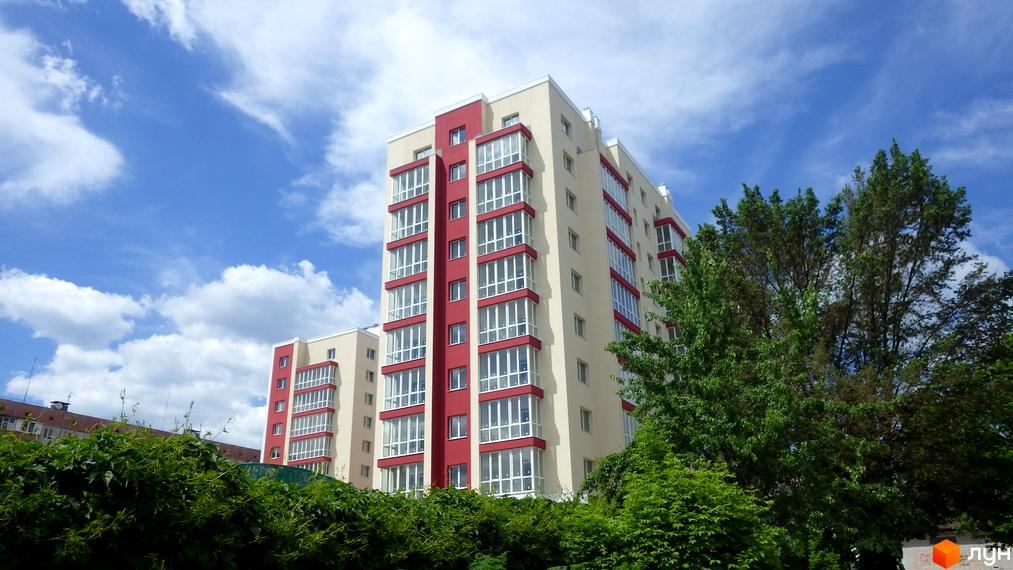 Житловий комплекс Мрія з бежево-червоними фасадами та заскленими балконами. Оточений зеленню під блакитним небом.