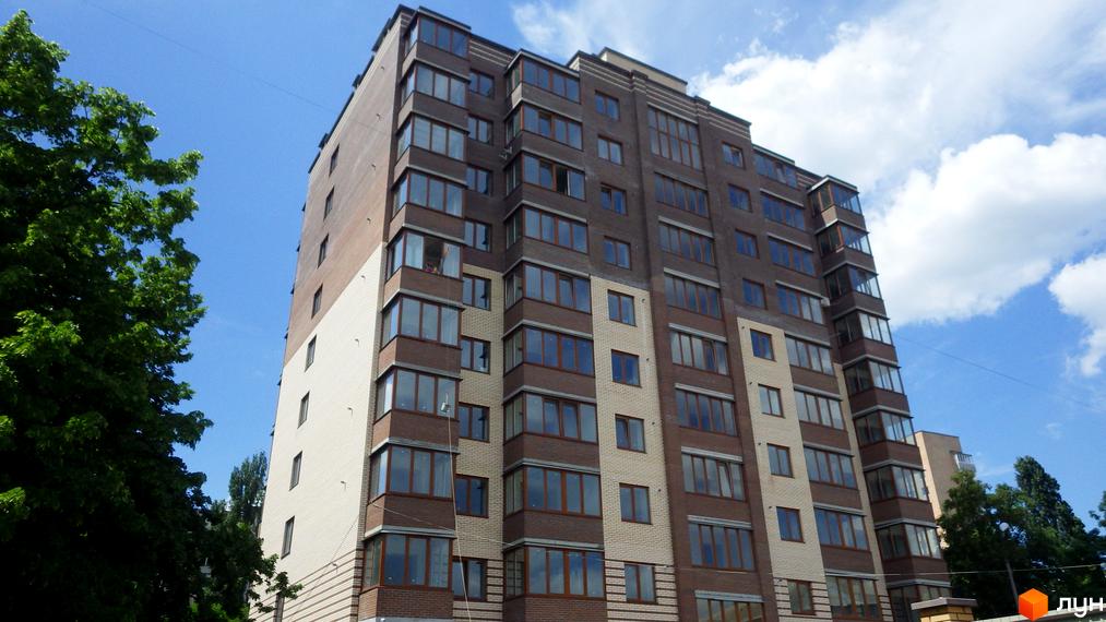 Житловий комплекс Аристократ: багатоповерховий будинок з коричневою та світлою цегляною обробкою, великими вікнами та зеленими деревами навколо.