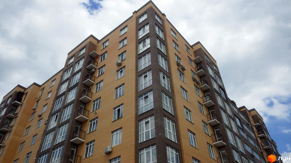 Зовнішній вигляд багатоповерхового будинку ЖК Зелений з жовтою та коричневою цегляною обробкою, численними вікнами та балконами. Навколо будинку видно елементи прибудинкової території.