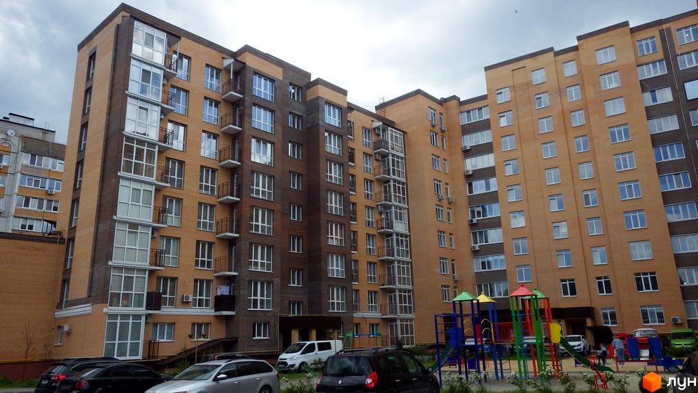 Зовнішній вигляд житлового комплексу Зелений з цегляним фасадом та численними вікнами. На прибудинковій території розташований дитячий майданчик.