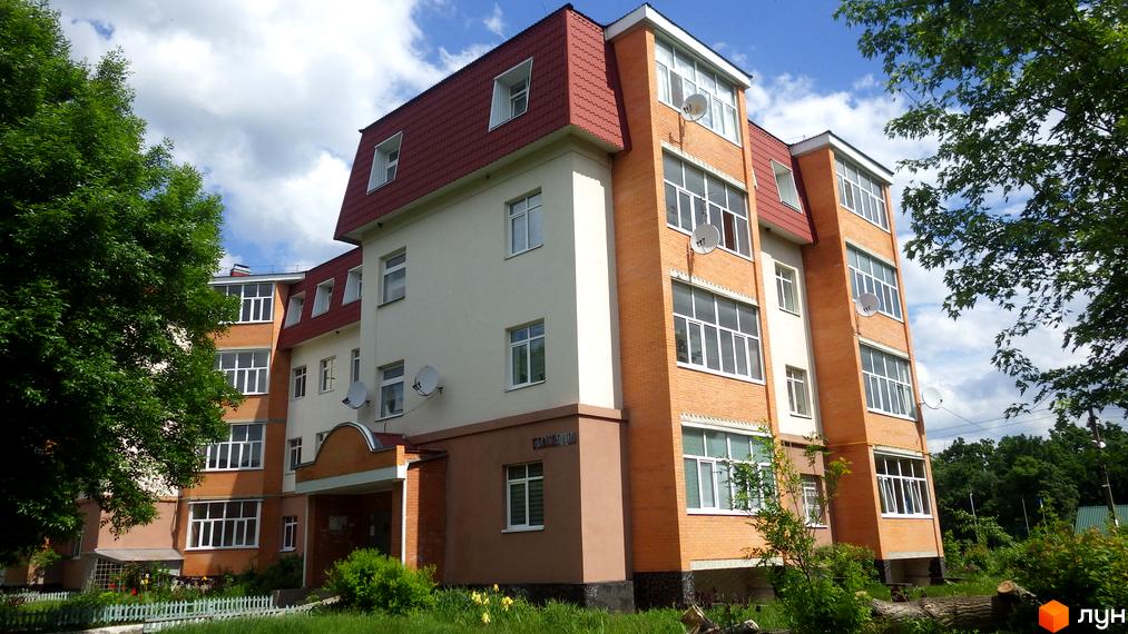 Житловий комплекс на вул. Гайок, 224б з помаранчевою цеглою та світлими стінами, червоним дахом. Навколо зелені дерева та доглянута прибудинкова територія.