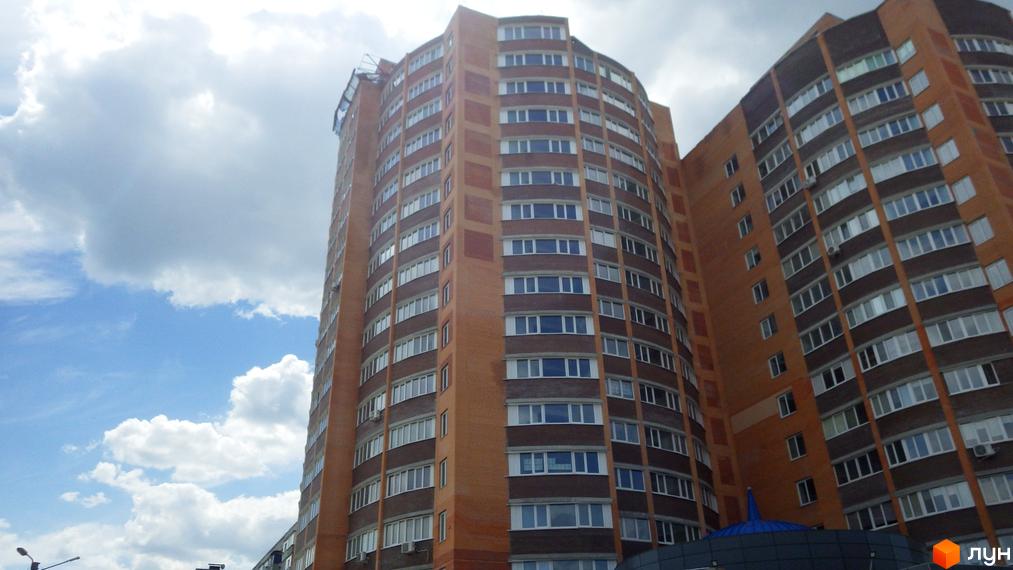 Висотна будівля житлового комплексу з цегляним фасадом на фоні хмарного неба. Вікна квартир виходять на сонячну сторону.