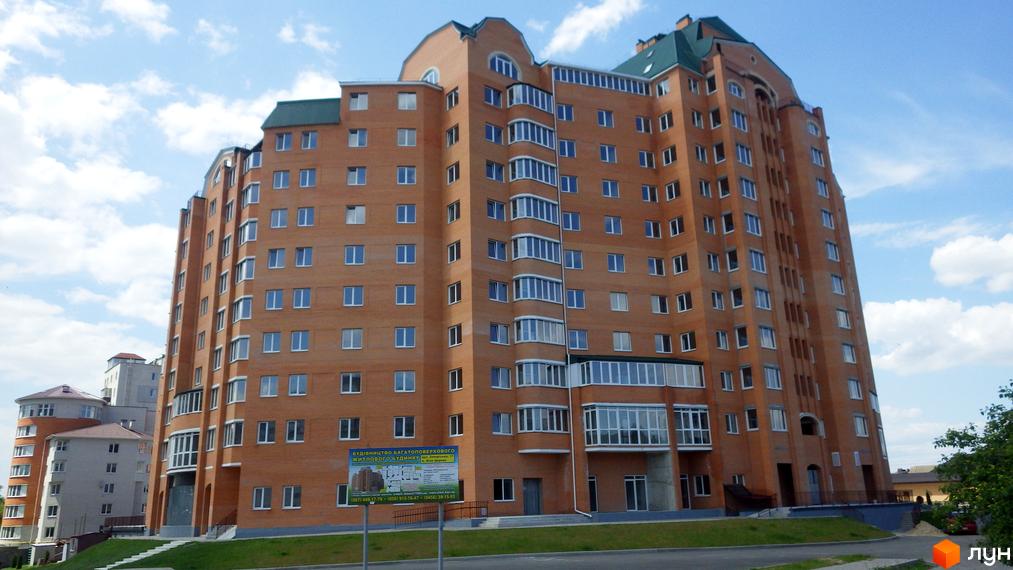 Багатоповерховий будинок з цегляною фасадною частиною. Поруч з будинком розташована прибудинкова територія з газоном та дорогою.