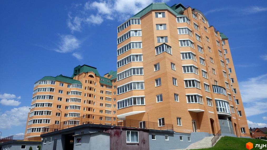 Високоповерховий будинок з цегляною кладкою на фоні блакитного неба. Біля будинку є зелена трава та невеликі будівлі.