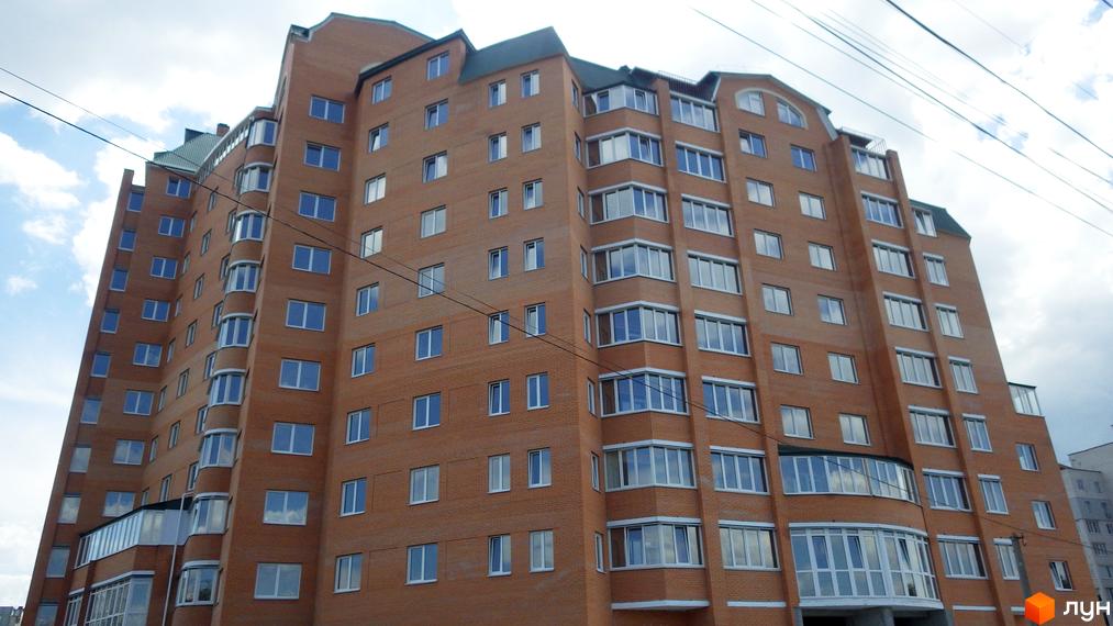 Висотна новобудова з цегляними фасадами та панорамними вікнами. Навколо будівлі видно лінії електропередач та небо з хмарами.