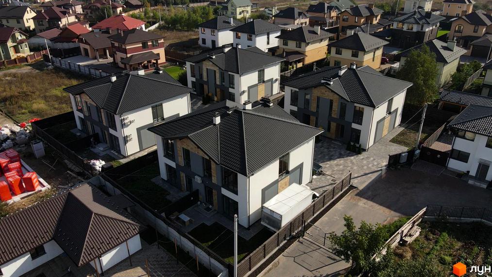 Зображення сторінки житлового комплексу Дуплекси Sandstone Comfort з двоповерховими будинками з темною покрівлею та прибудинковою територією з газонами та парканами.