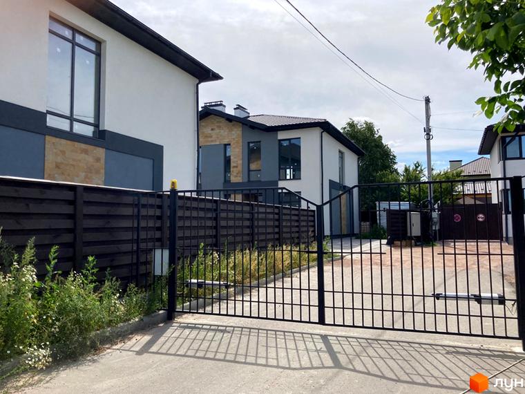 Двоповерхові будинки з білими стінами та темною покрівлею в Котеджному комплексі Sandstone Comfort. На території котеджів встановлено металеву огорожу та ворота.