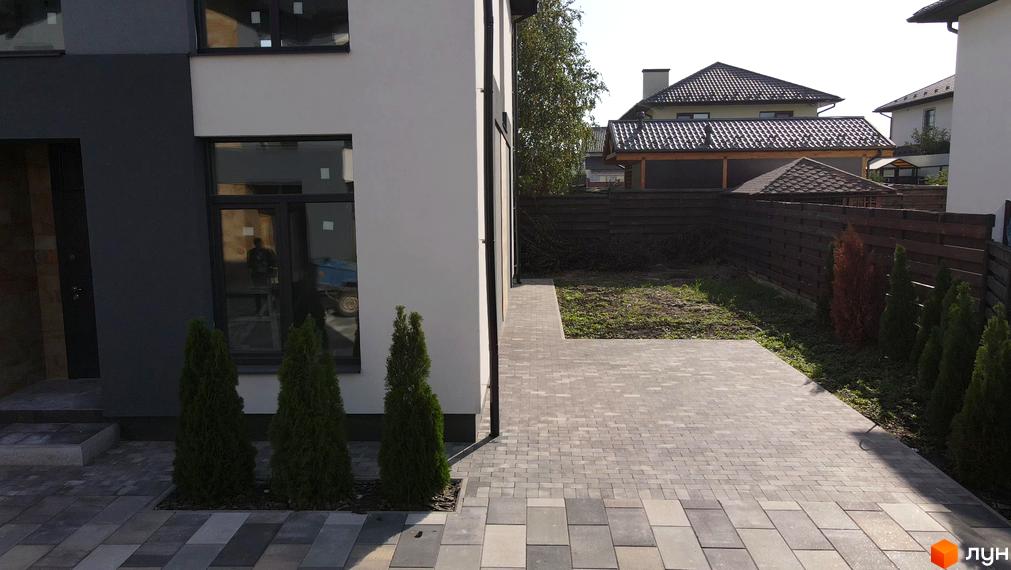 Фасад будинку в ЖК Sandstone Comfort з великими вікнами та доглянутою прибудинковою територією, вимощеною плиткою.