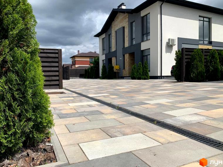 Двоповерховий будинок з білими стінами та темним дахом в ЖК Sandstone Comfort. Простора прибудинкова територія з бруківкою та зеленими насадженнями.