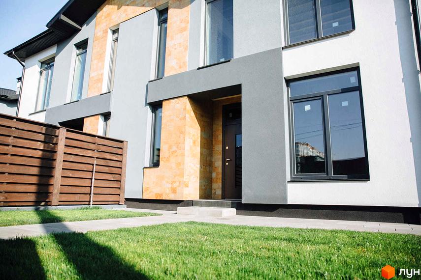 Фасад будинку ЖК Sandstone Comfort з великими вікнами та оздобленням з каменю. Перед будинком газон та доріжки з тротуарної плитки.