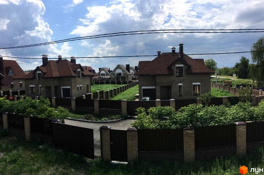 Котеджне містечко КМ Барвіта: двоповерхові будинки з коричневими дахами та парканами навколо території. Зелена прибудинкова територія з деревами та кущами.