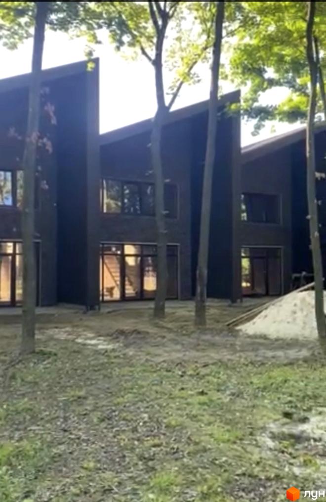 Таунхаус Forest Park Gora з темними фасадами та великими вікнами, оточений деревами. Прибудинкова територія з газоном та піском.