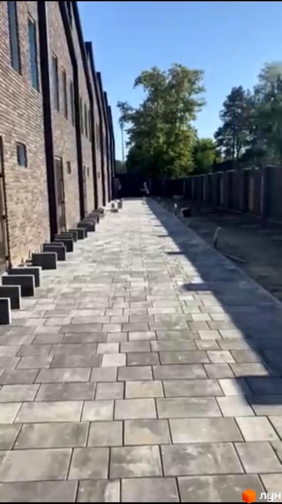 Зовнішній вигляд таунхаусів Forest Park Gora з бруківки та зеленої зони. Комплекс розташований біля дерев.