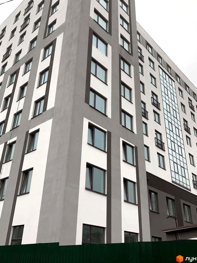 Зовнішній вигляд житлового комплексу Вільський з сірими та білими фасадами та великою кількістю вікон. На передньому плані зелений паркан.