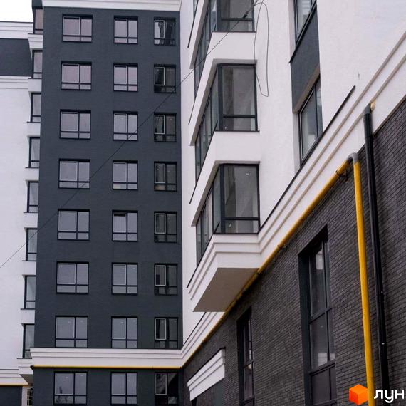 Зовнішній вигляд новобудови ЖК Вільський з темною цегляною кладкою та білими елементами фасаду. Вікна з темними рамами та балконні виступи.