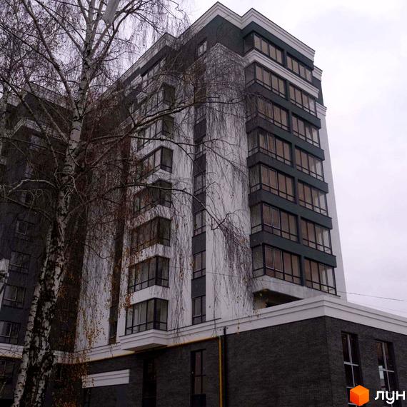 Новобудова ЖК Вільський має сіро-білий фасад з великими вікнами. Навколо будівлі видно дерева з голим гіллям.