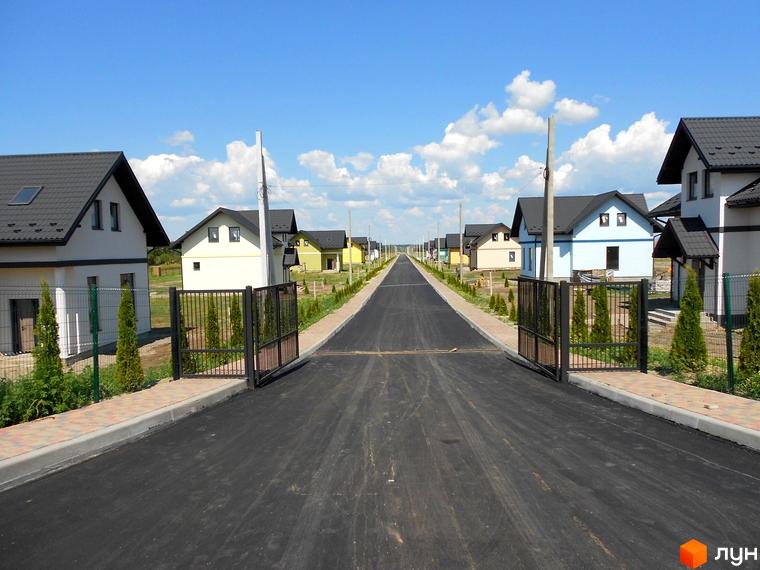 Котеджне містечко КМ Лелека: нові будинки з сірими дахами та парканами вздовж асфальтованої дороги з зеленими насадженнями.