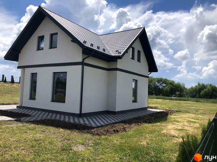 Котеджне містечко КМ Лелека: двоповерховий будинок з білими стінами, темним дахом та вікнами, розташований на зеленій ділянці з бруківкою.