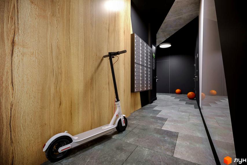 Сучасний вхід у ЖК OBRIY3 з дерев'яною обшивкою стін та зручною зоною для зберігання самокатів. Стильна підлога та освітлення створюють затишну атмосферу.